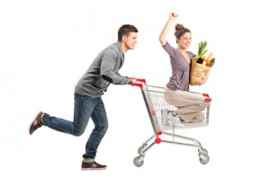 Person pushing a happy woman in a shopping cart with paper bag f