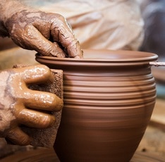 Potter hands making in clay on pottery wheel.