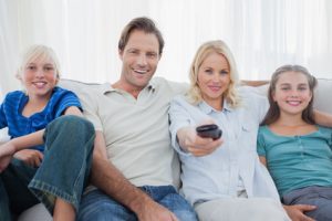 Parents posing with children and watching television sitting on a couch